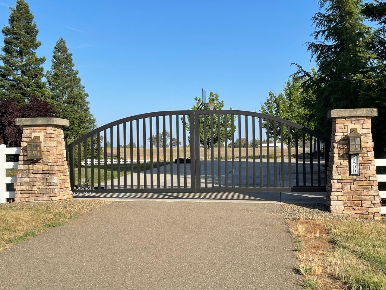 Elegant arched wrought iron driveway gate with stone columns installed by Automatic Gate Mates in Bay Area countryside