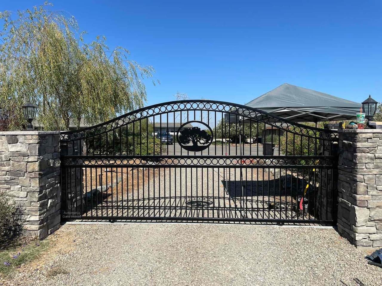Decorative wrought iron driveway gate with custom tree emblem and stone columns installed by Automatic Gate Mates in Bay Area