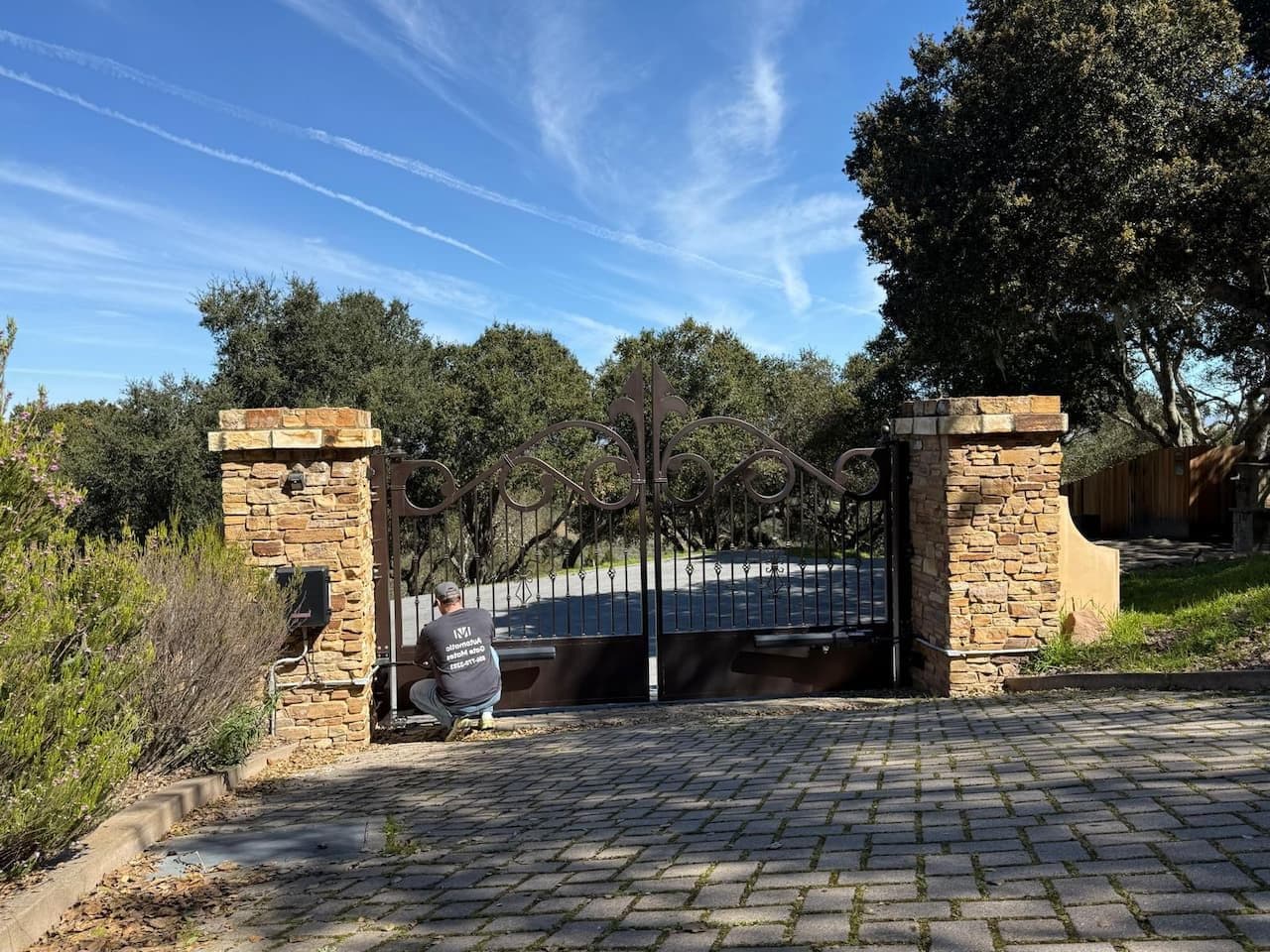 Automatic Gate Mates technician performing service on decorative wrought iron gate with stone columns in Bay Area