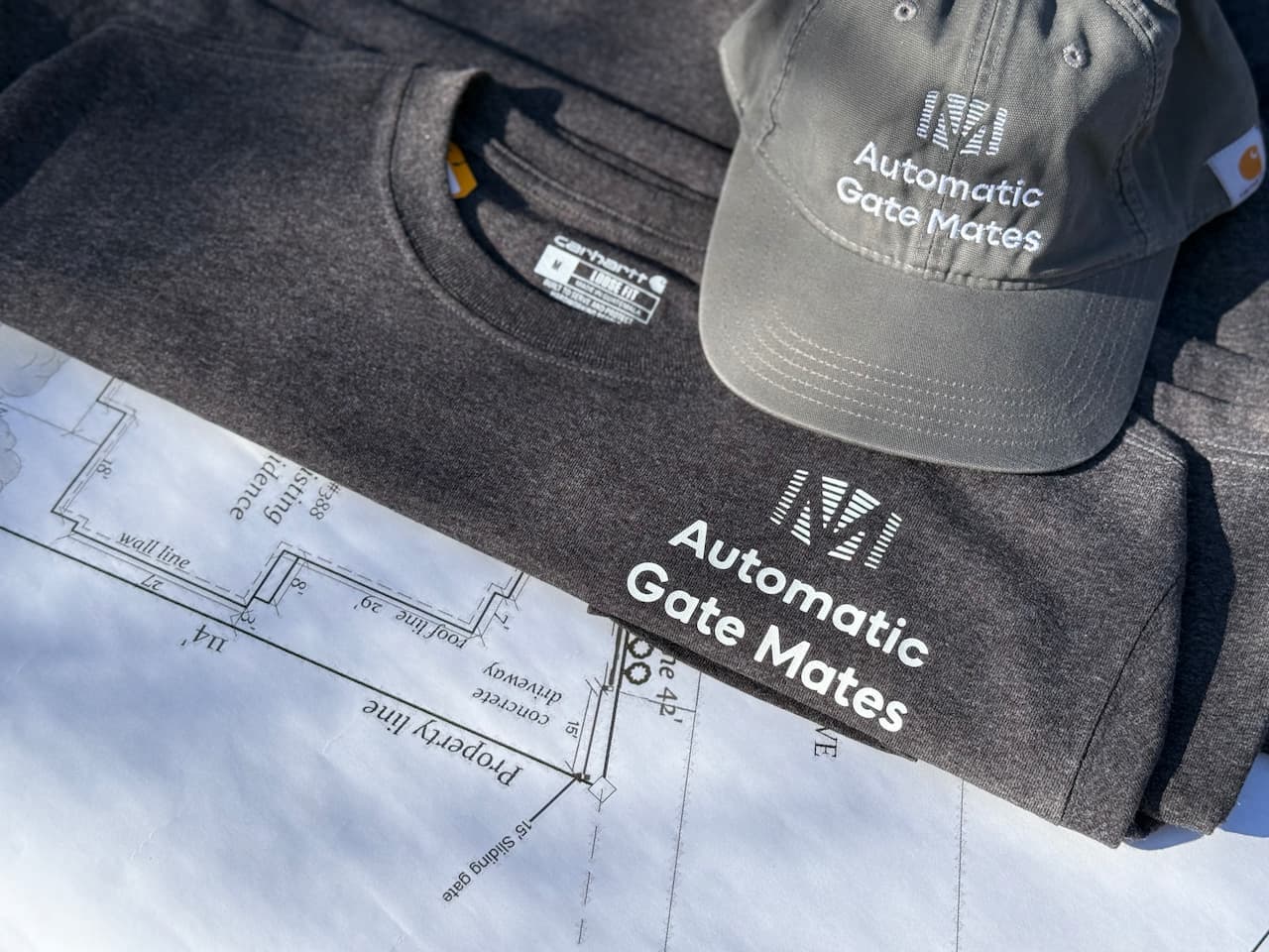 Automatic Gate Mates branded uniform and cap on project blueprint showcasing professional gate installation services in the Bay Area